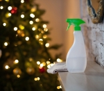 A hand in a yellow glove holds a bottle of detergent against the background of New Year's lights. General professional cleaning before Christmas. Spray disinfection